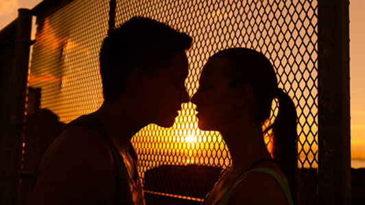 two people about to kiss in front of fence