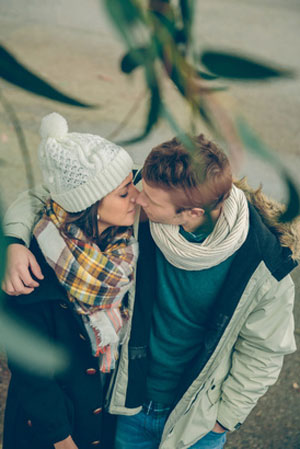 warmly dressed couple kissing near leaves