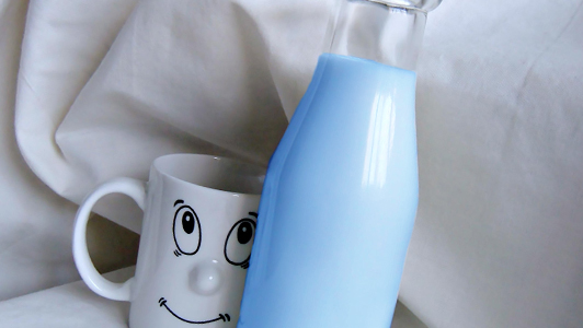 A bottle with blue milk and white mug with a smiling face on it.