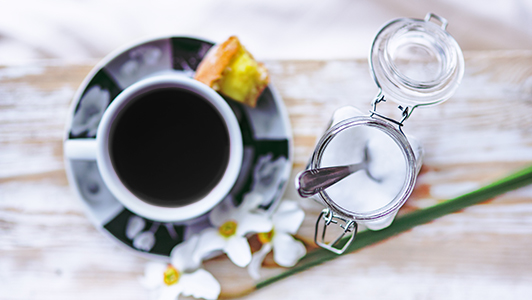 A cup of black tea, jar with sugar and a flower.