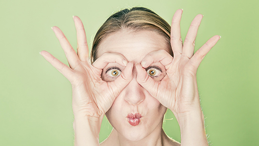 Woman making funny faces and holding her hands shaped like glasses.