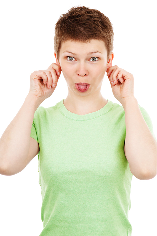 A woman in gray shirt holding her ears and sticking her tongue out.