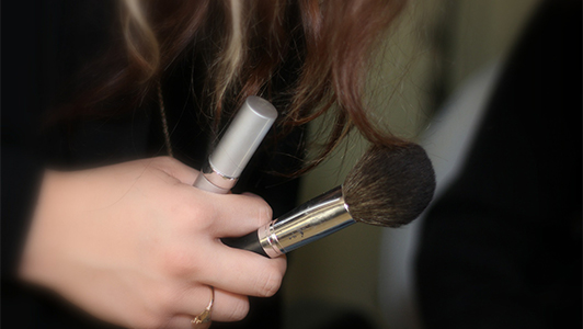 Girl holding a makeup brush and lipstick.