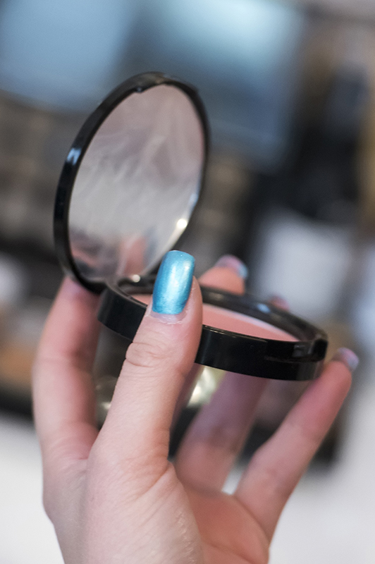 Girl with blue nails holding pressed powder.