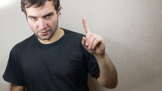 Guy in a black tee shirt holding his finger raised.