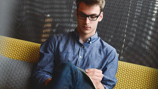 Guy with glasses and denim shirt writing something down.