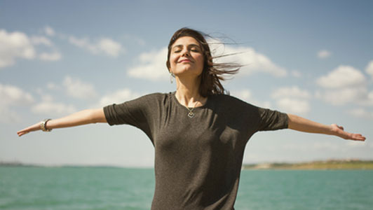 women with arms wide open closing eyes while breathing fresh air