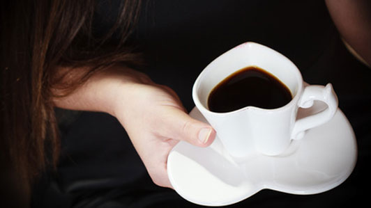 hand of woman on heart cup filled with coffee