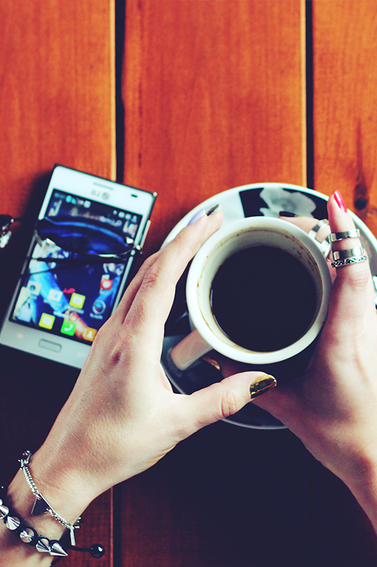 Girl with interesting jewelry holding a cup of coffee.