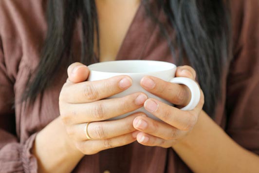 women in brown wearing a ring holding a cup of coffee with both hands 