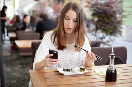 woman texting while eating sushi