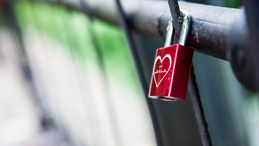 Red padlock with white heart attached to a gate.