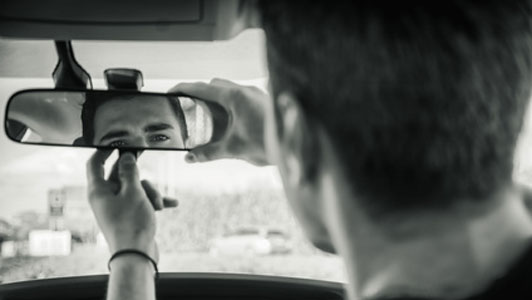 man looking at self in rear view mirror