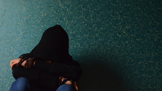 Guy with black hoodie resting his head on his crossed arms.