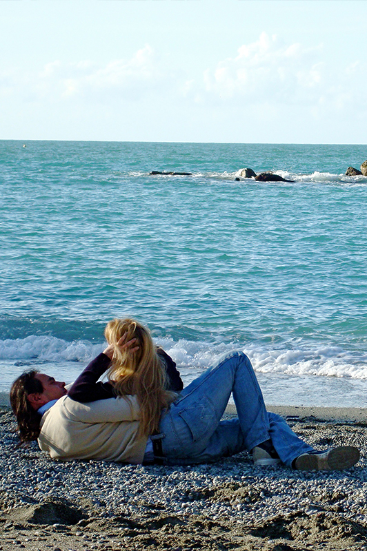 Man in jeans and sweater lying on a beach with a blonde girl.