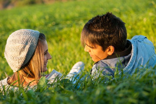 Couple laying in grass field at sunset.