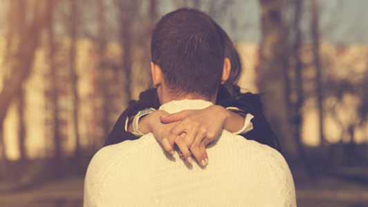 man and woman hugging around trees