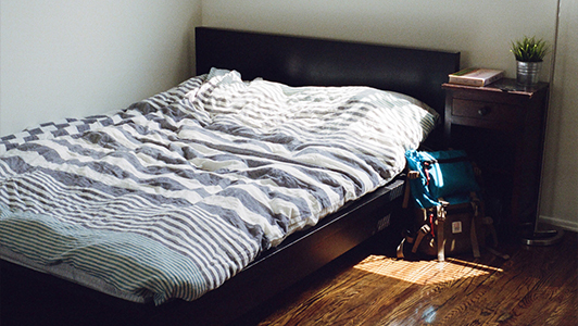 Black bed with duvet on stripes and two bags left on the floor.