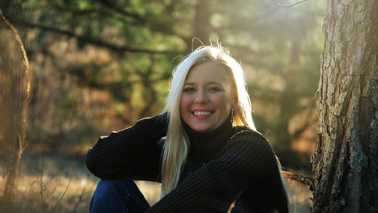 Blonde girl in black sweater sitting in the woods.