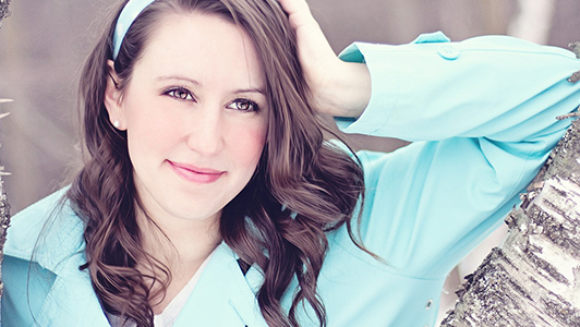 Brunette girl in a blue coat leaned against a tree.