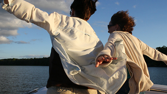 A couple in white jackets holding their arms spread while on a boat.