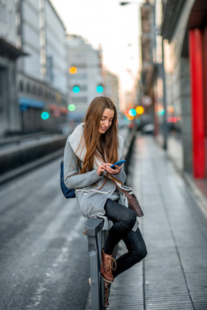 young woman sitting on rail texting