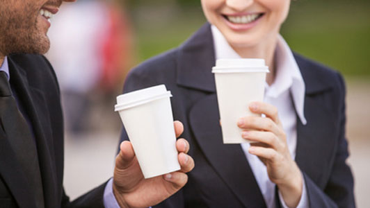 To mennesker med kaffekopper i hånden smilende