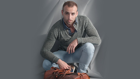 Guy in a gray sweater with a brown bag in front of him.