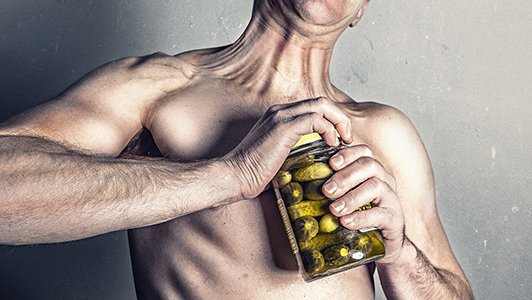 A guy having hard time opening a jar of pickles