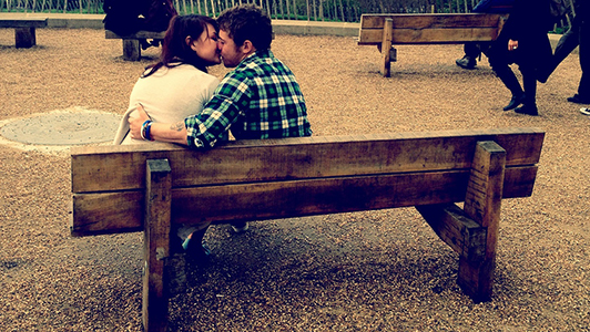A couple sitting on a wooden bench and kissing.