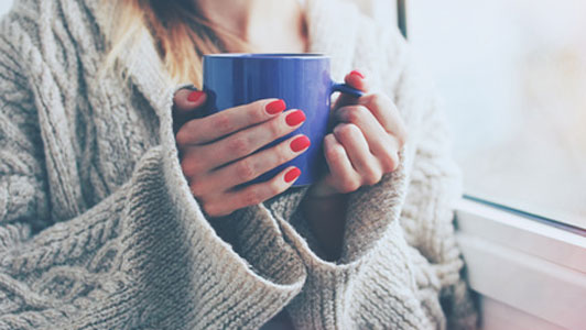 woman in sweater holding blue coffee mug
