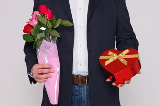 guy holding flowers and heart shaped box of chocolates