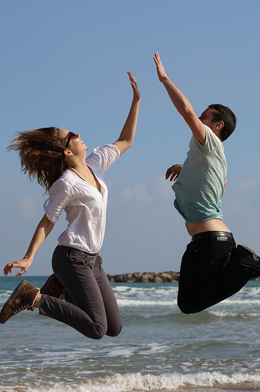 Guy and a girl jumping in the air and giving each other a high five.