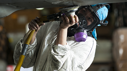 Girl with a mask and white protection suite using a tool.