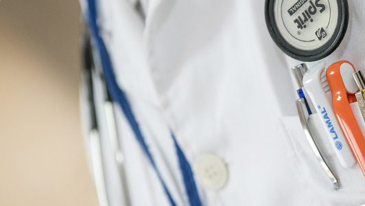 A close up of a doctor's stetoscope, and pens in his pocket.