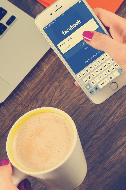 Girl logging in to facebook while holding a cup of coffee.