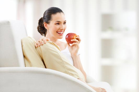 mujer sentada en un sofá comiendo una manzana en un fondo blanco