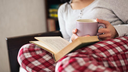 women in pajamas reading book over cup of tea