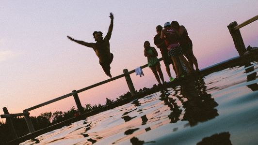 Friends hanging out by the pool while one jumps in the water