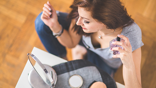 Girl looking herself in the mirror and putting on perfume.