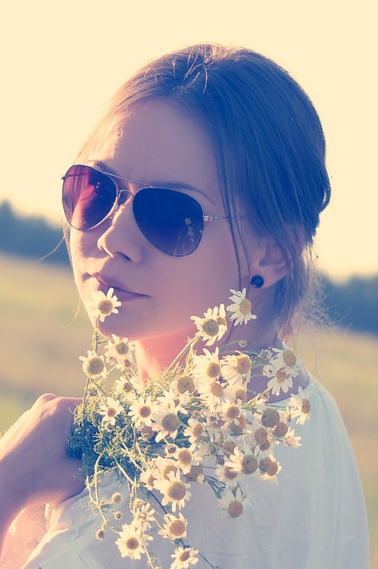 Girl with sunglasses holding flowers.