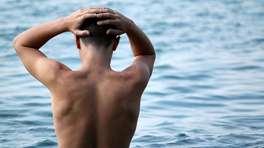 Guy standing in water and holding his head with his hands.