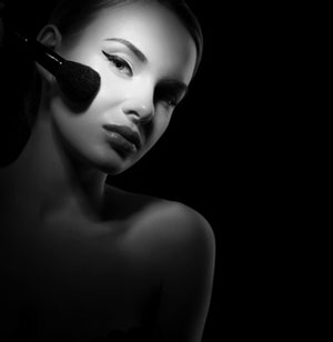 black and white image of woman applying blush on cheek