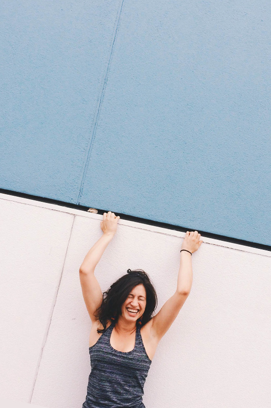 Girl leaned against a wall laughing.