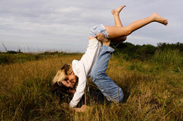 A blond girl kissing a guy lying in the field.