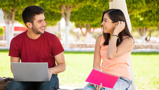 woman sitting in courtyard with guy on laptop flicking hair back