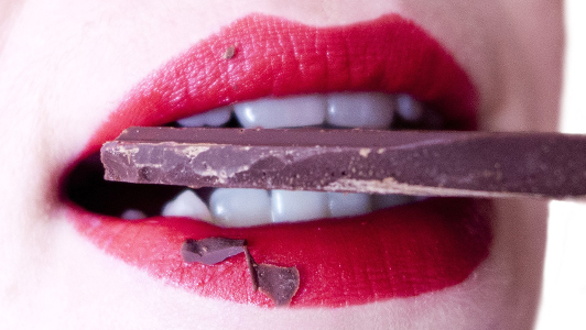 Girl holding a piece of chocolate between her teeth.