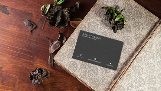 Black business card in a notebook, dry flowers placed around it.