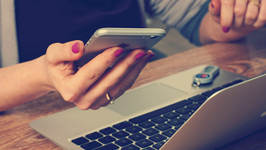 Girl sitting in front of a laptop and holding an iPhone.