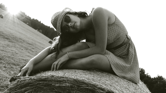 Girl in a dotted dress and a hat sitting on a bale of hay